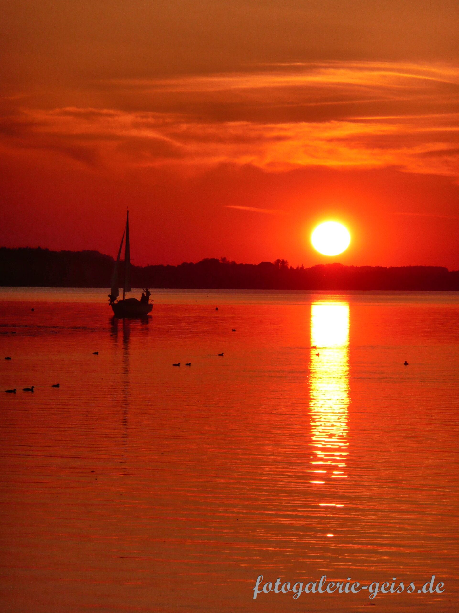 Sonnenuntergang über dem Chiemsee mit Segelboot